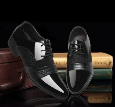 Pair of stylish black and white men's formal dress shoes displayed with stacked vintage books and a leather suitcase