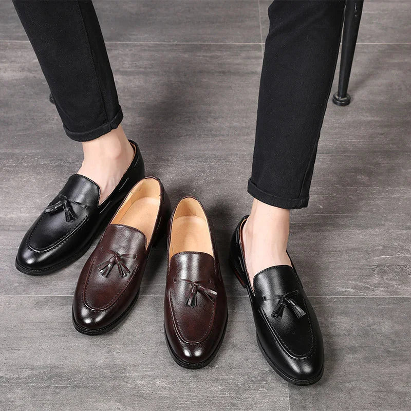 Men's tassel loafers in black and brown leather on gray floor with model wearing black pants