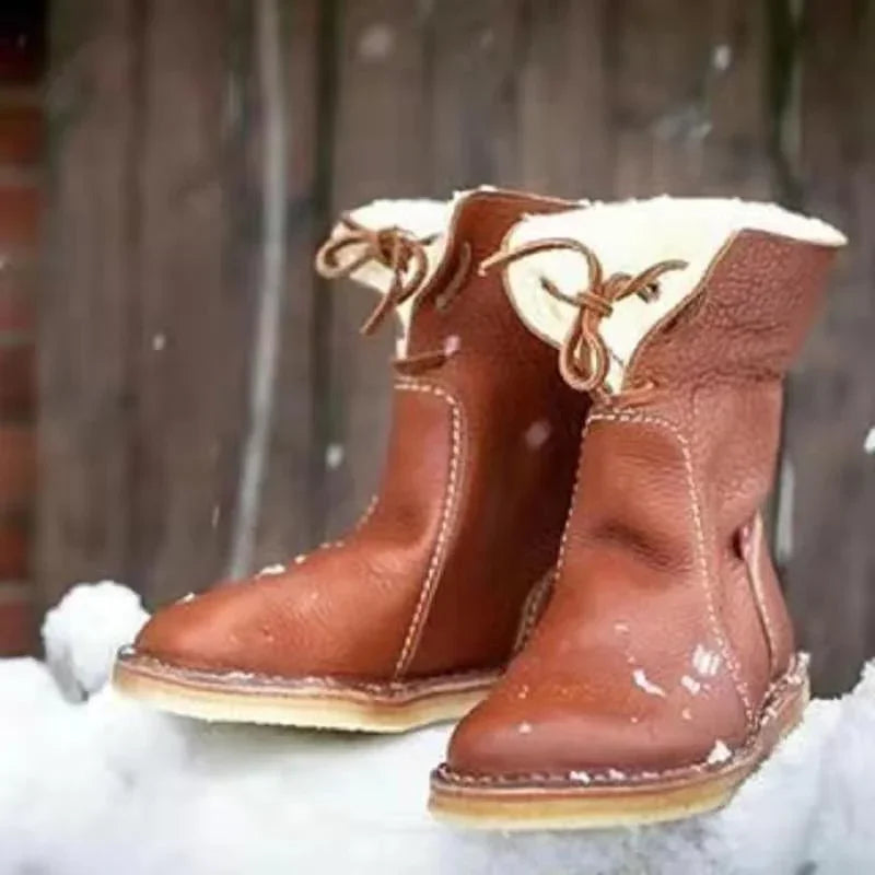 Brown leather winter boots with white fur lining on snowy surface against rustic wooden background