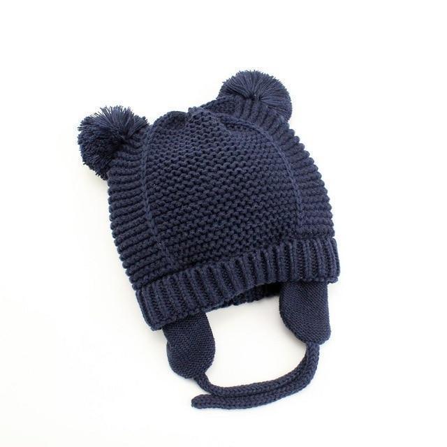 Navy blue knitted winter hat with ear flaps and two pom-poms on white background