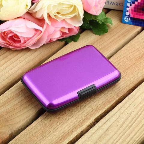 Compact purple metal wallet case on wooden surface with pink and white roses nearby