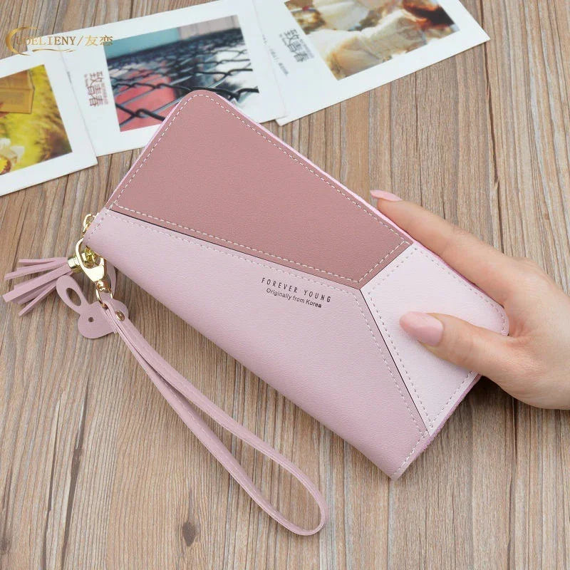 Pink geometric leather wallet with wrist strap and tassel charm on wooden surface