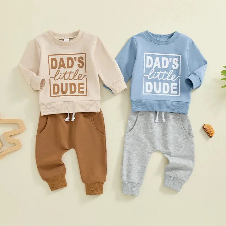 Two toddler outfits with "Dad's little dude" tops in beige and blue paired with brown and gray pants