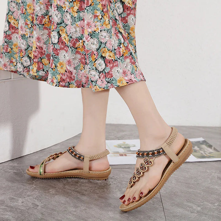 Woman wearing beige embellished flat sandals with floral patterned midi skirt on gray floor