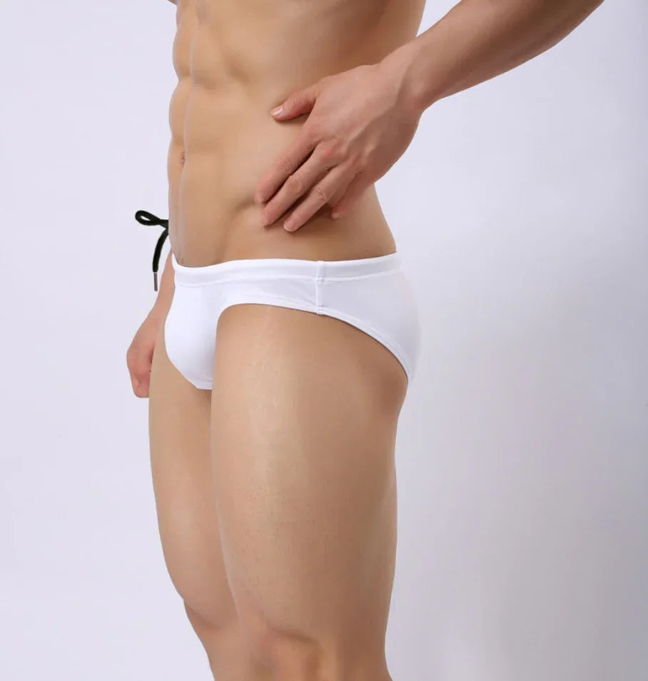 Close-up of a man wearing white swim briefs with black drawstring against a plain background