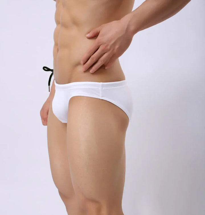 Close-up of a man wearing white swim briefs with black drawstring against a plain background
