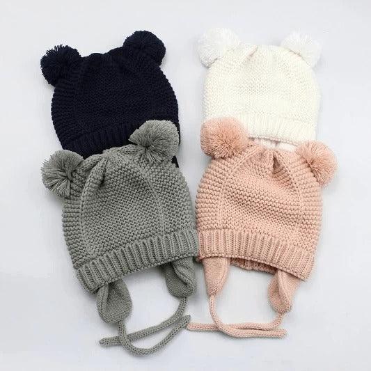 Four knitted baby hats with bear ears in black, white, gray, and pink colors on a white background