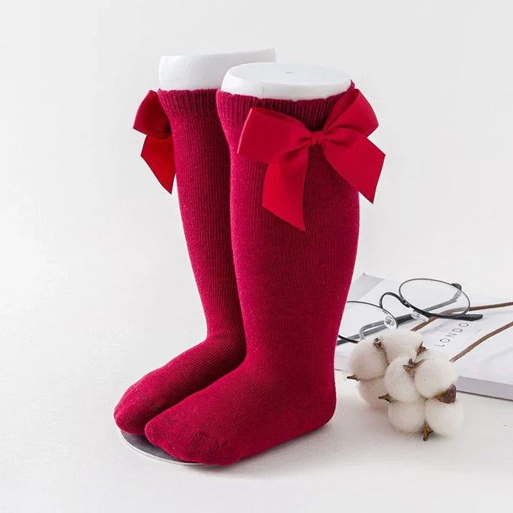 Pair of vibrant red knee-high socks with large red bows displayed on white mannequin feet