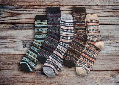 Five pairs of patterned wool socks in various earthy tones laid out on rustic wooden surface