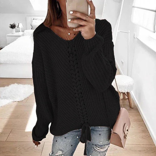 Woman wearing black knitted sweater with lace-up front detail and ripped jeans in modern bedroom