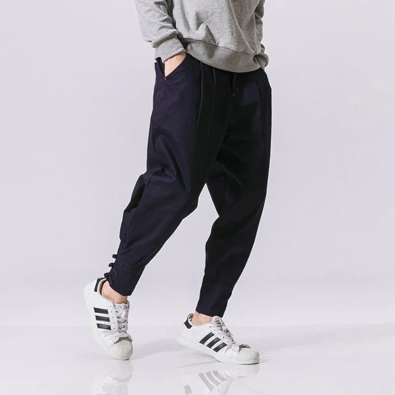 Person wearing black casual jogger pants and white Adidas sneakers with black stripes