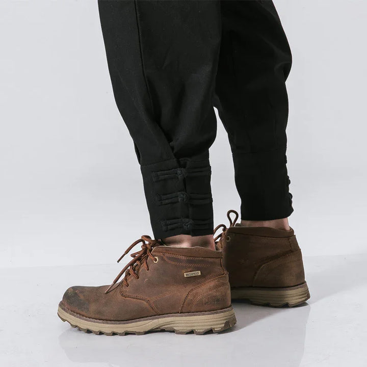 Brown waterproof leather boots paired with black tapered pants having button details on ankles