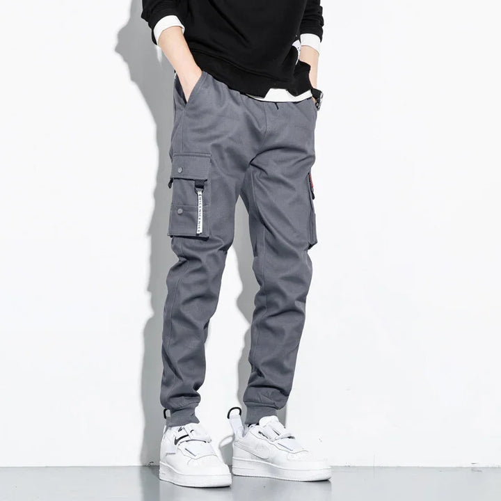 Man wearing gray cargo pants with multiple pockets and white sneakers on a white background