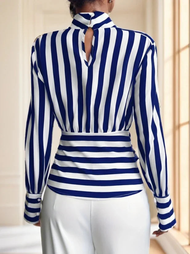 Woman wearing a blue and white vertical striped blouse with a keyhole back and white pants indoors