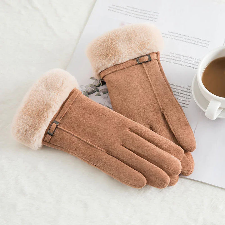 Pair of brown suede winter gloves with plush fur cuffs on a white surface beside a coffee cup