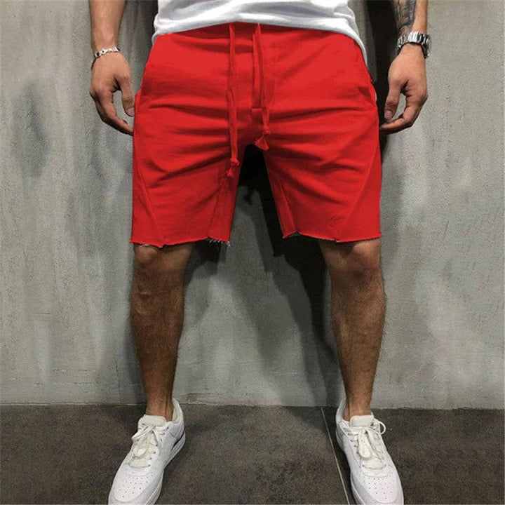 Man wearing bright red drawstring shorts and white sneakers standing against a gray concrete wall