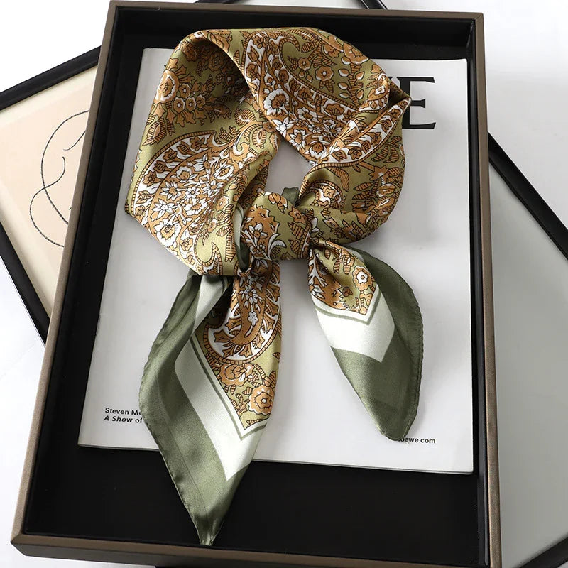 Silk scarf with paisley and floral pattern in green, white, and gold tied in a bow, displayed in a black tray