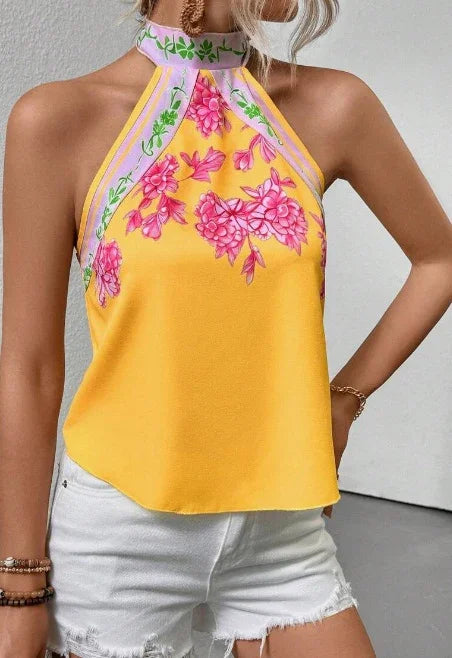 Woman wearing sleeveless yellow halter top with pink floral design paired with white distressed shorts