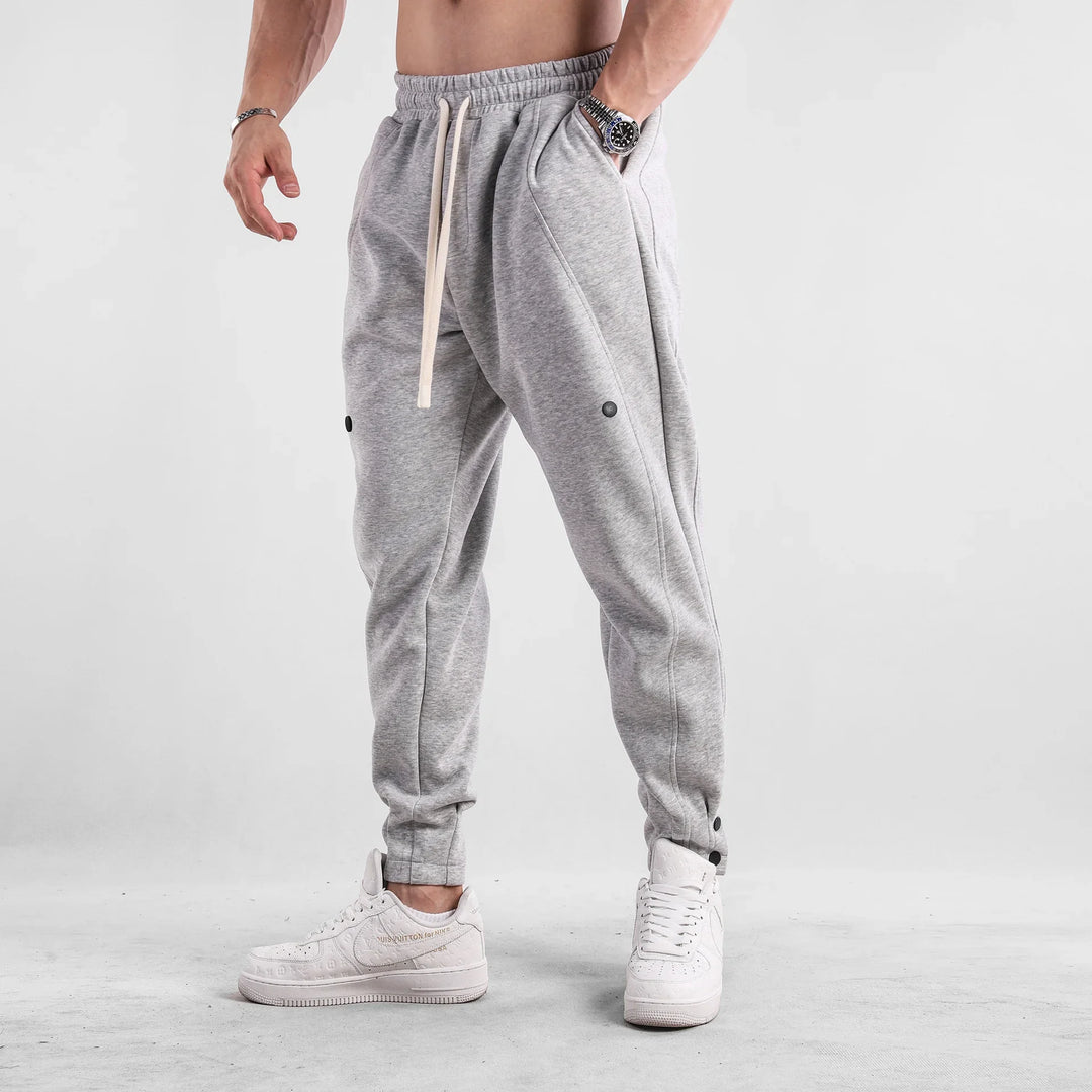 Man wearing light gray jogger pants and white sneakers on gray floor with white background