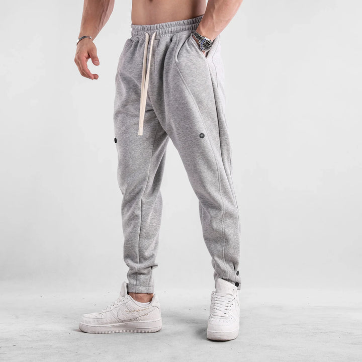 Man wearing light gray jogger pants and white sneakers on gray floor with white background