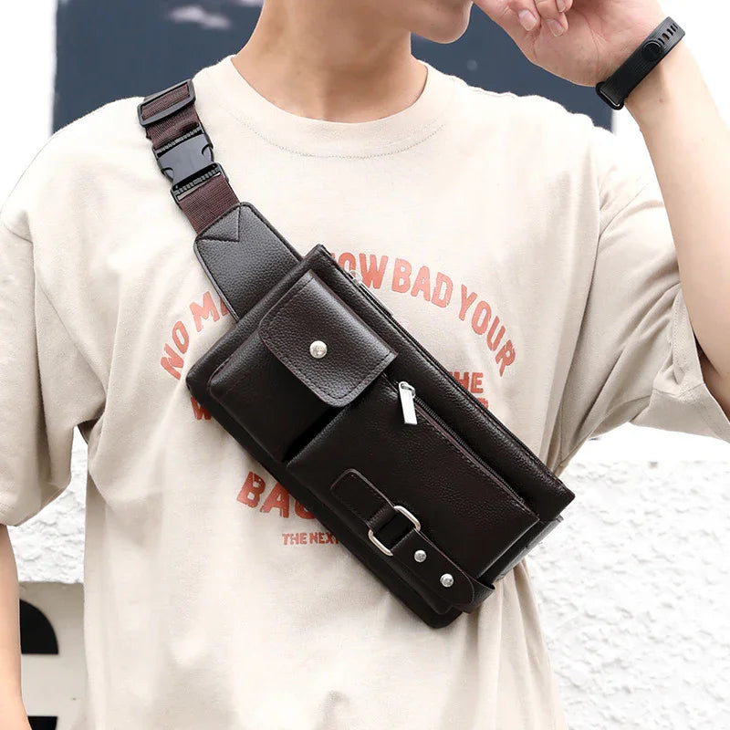 Person wearing beige graphic T-shirt with dark brown leather crossbody bag featuring zipper and buckle details