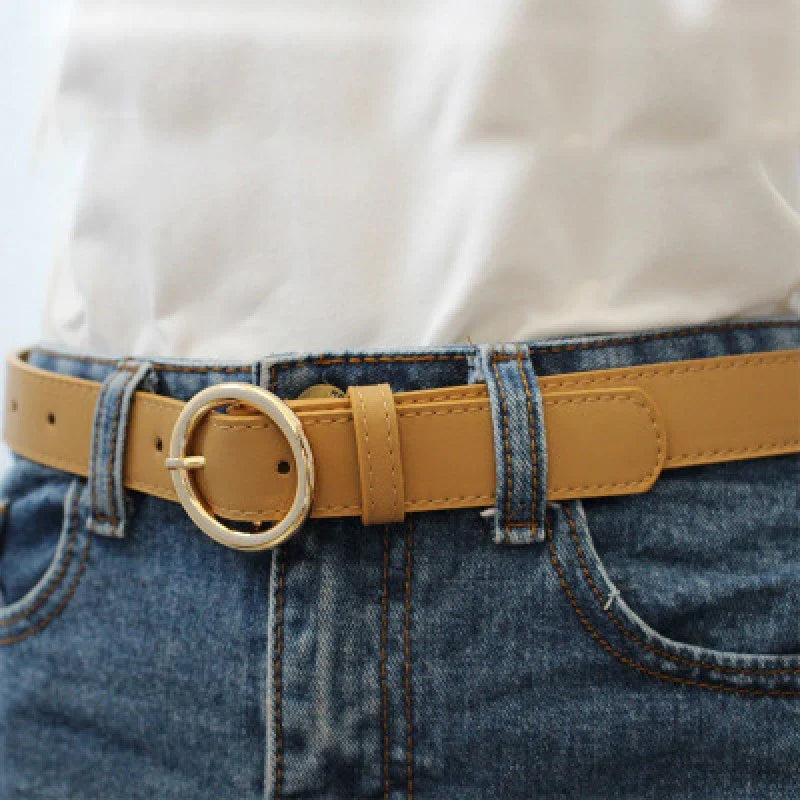 Close-up of tan leather belt with round gold buckle worn with blue denim jeans and white shirt