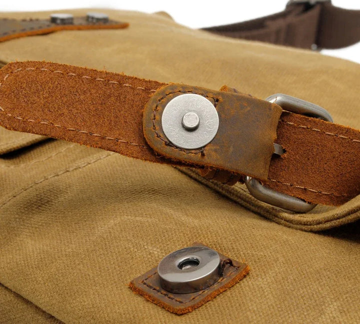 Close-up of vintage canvas bag with brown leather strap and metal button snap closure