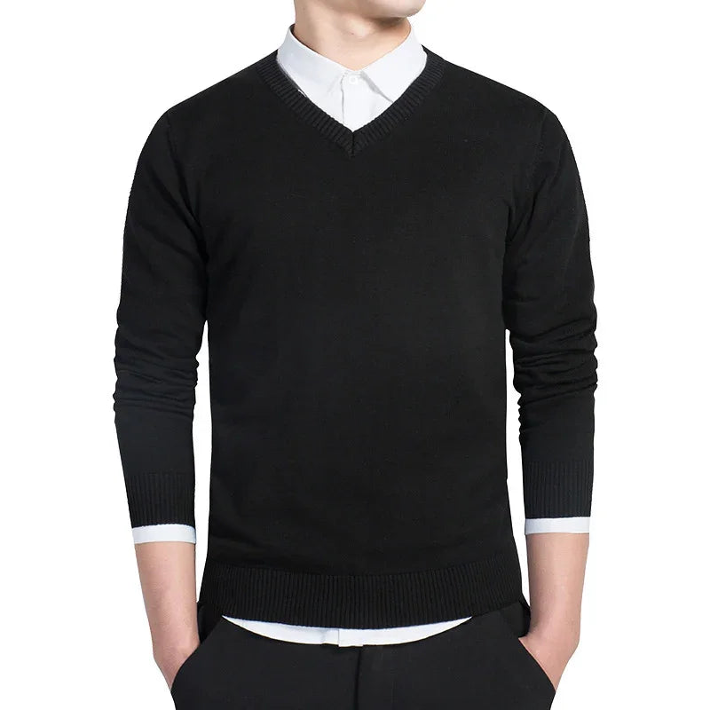 Man wearing black V-neck sweater over white dress shirt with hands in pockets