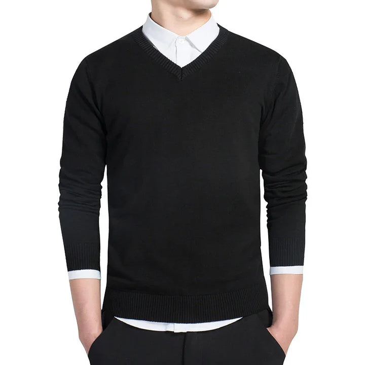 Man wearing black V-neck sweater over white dress shirt with hands in pockets