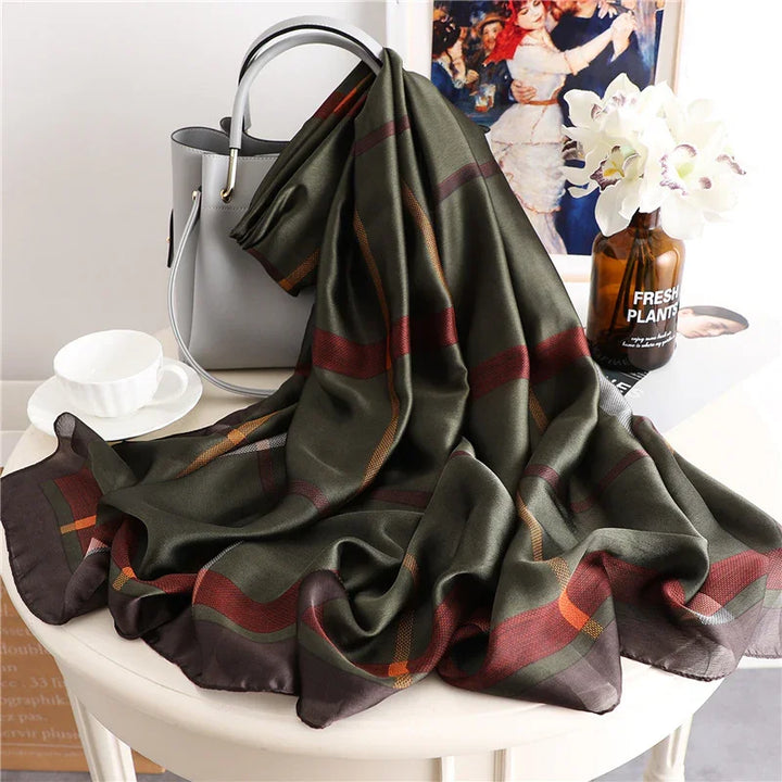 Olive green silk scarf with red and orange stripes on white table beside gray handbag, teacup, and flower vase
