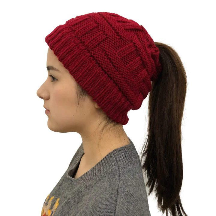 Side view of woman wearing red knit ponytail beanie hat with long dark hair and gray sweater