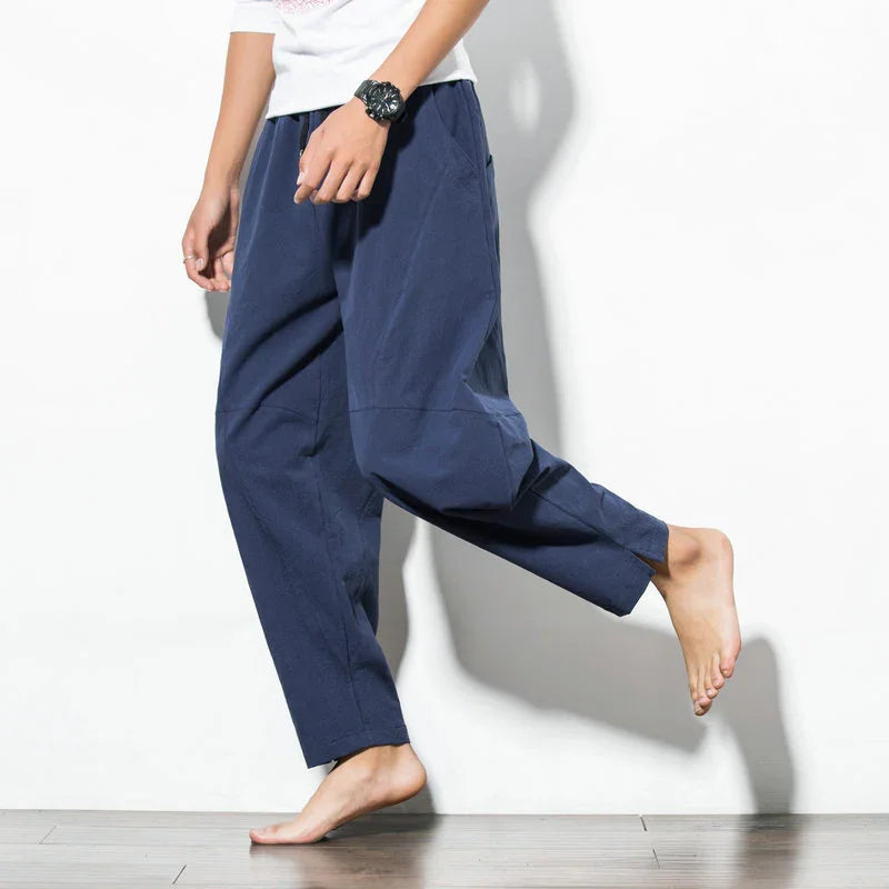 Person wearing loose navy blue casual pants walking barefoot on wooden floor against white wall