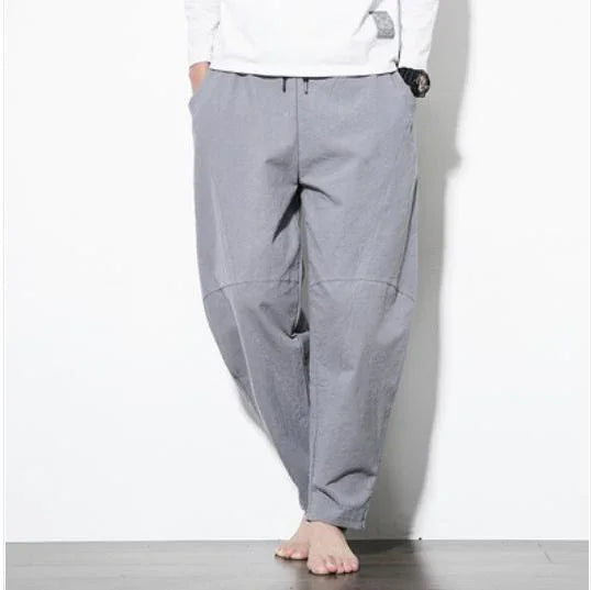 Person wearing casual light gray loose drawstring pants and white long-sleeve shirt, barefoot against white wall