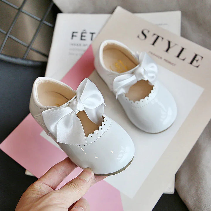 Close-up of white baby shoes with satin bows on top, placed on fashion magazines