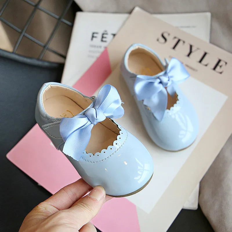 Baby blue patent leather toddler shoes with scalloped edges and large satin bows on style magazines
