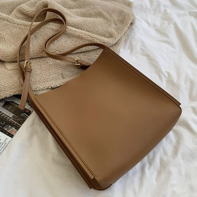 Minimalist brown leather shoulder bag with adjustable strap on beige fleece fabric and white surface