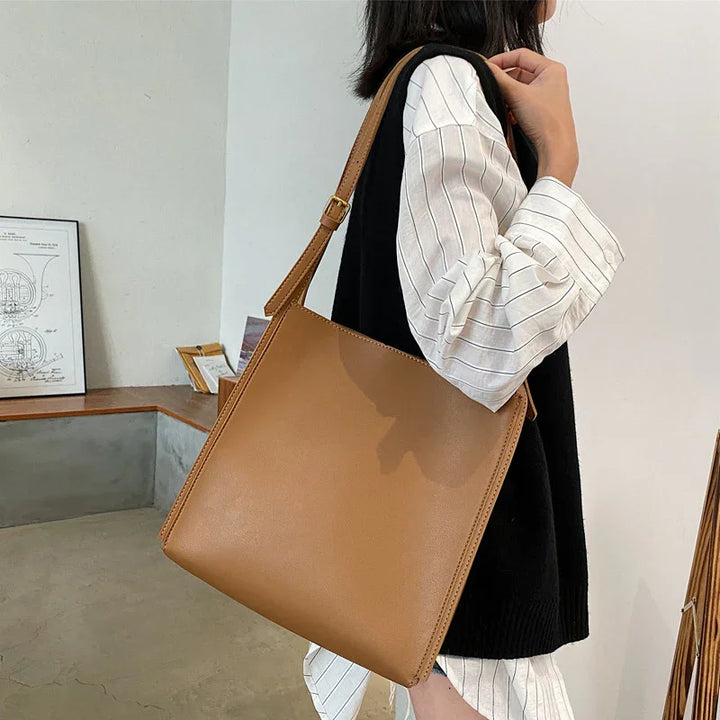 woman wearing black vest and white shirt holding large tan leather shoulder bag indoors