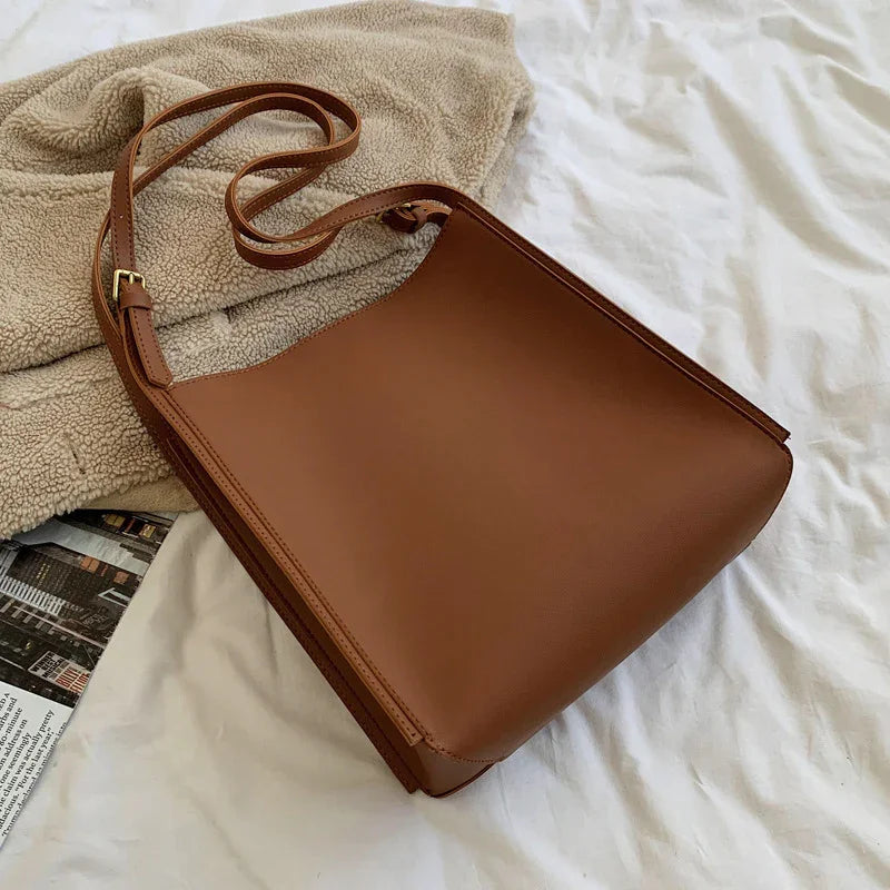 Brown leather shoulder bag with adjustable strap on beige fleece jacket and white fabric background