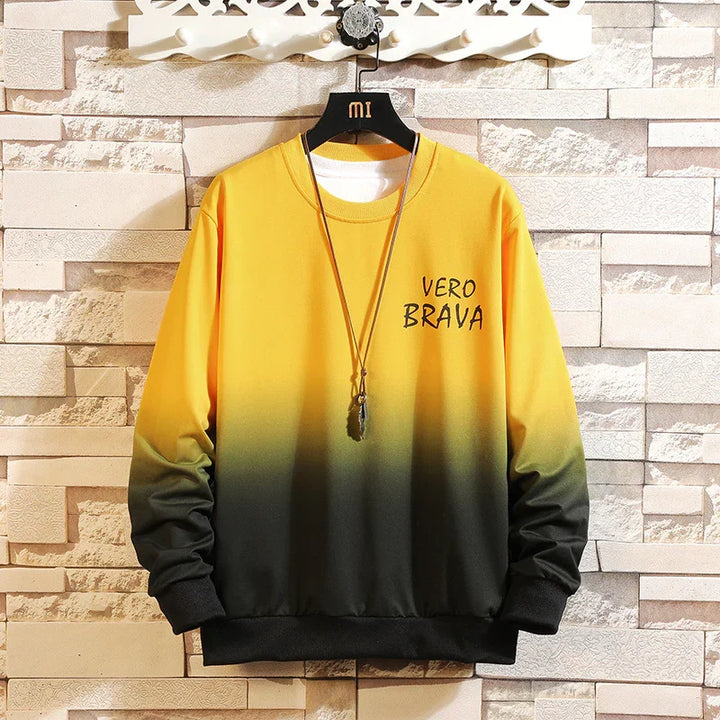 Yellow to black gradient sweatshirt with 'VERO BRAVA' text hanging on black hanger against beige stone wall