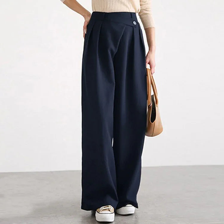 Woman wearing navy blue wide-leg pants, beige sweater, white sneakers, holding tan handbag