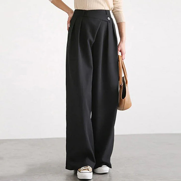 Woman wearing high-waisted black wide-leg pants with beige top and white sneakers holding tan handbag