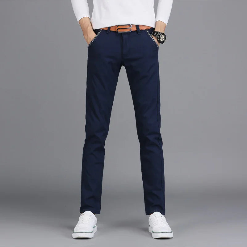 Men's slim fit navy blue casual pants with brown belt and white sneakers on gray background