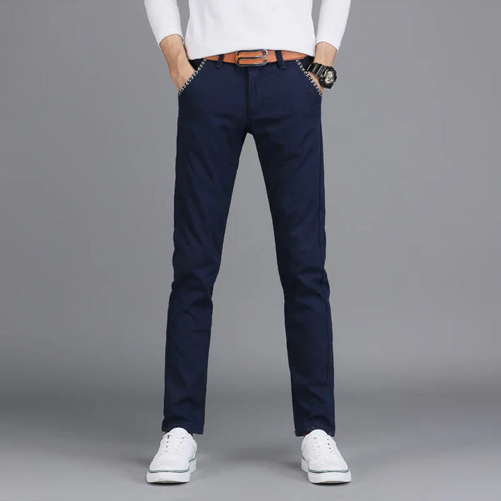 Men's slim fit navy blue casual pants with brown belt and white sneakers on gray background