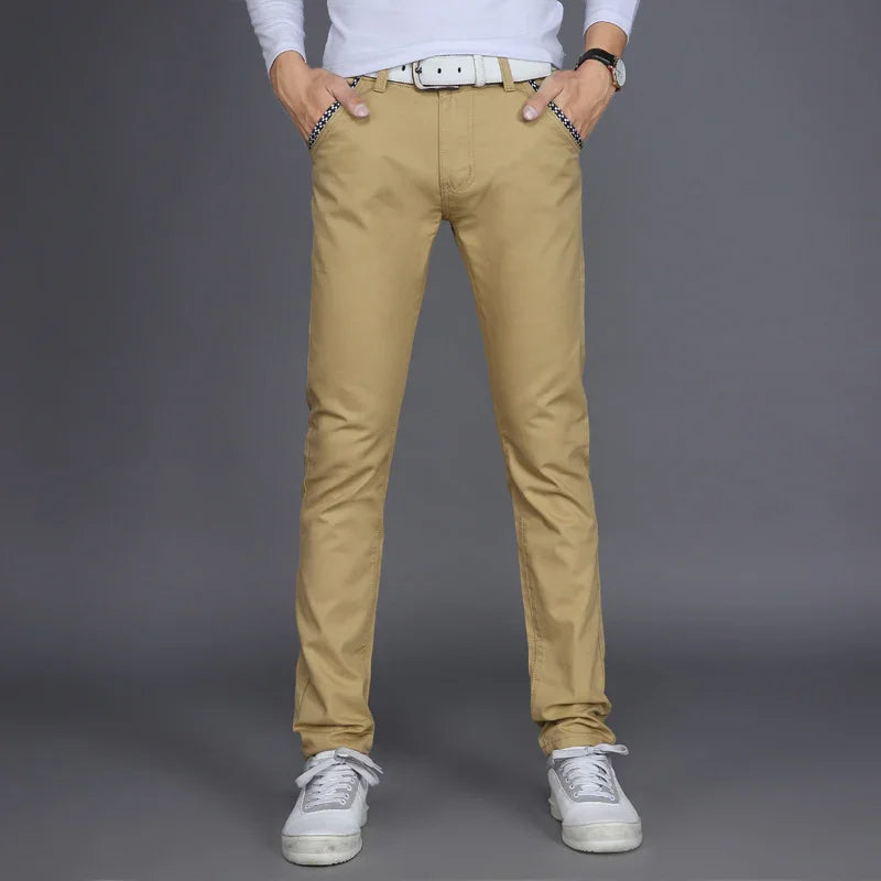 Man wearing beige slim-fit chinos with white belt and gray sneakers on gray background