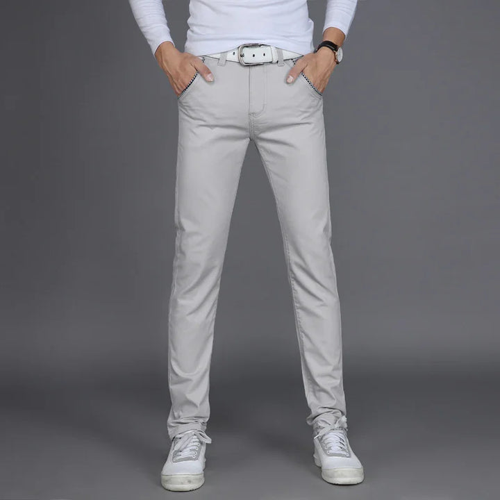 Man wearing light gray slim-fit pants with white belt, white sneakers, and a white long-sleeve shirt