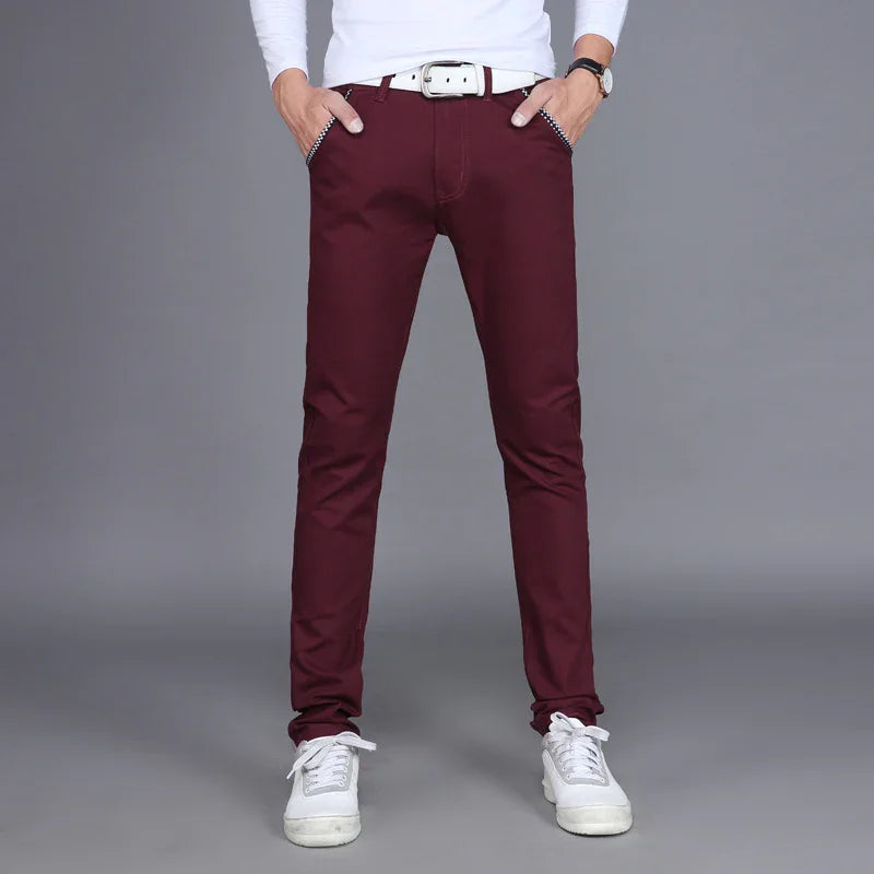 Man wearing slim fit maroon pants with white belt, white long sleeve shirt, and white sneakers on gray background