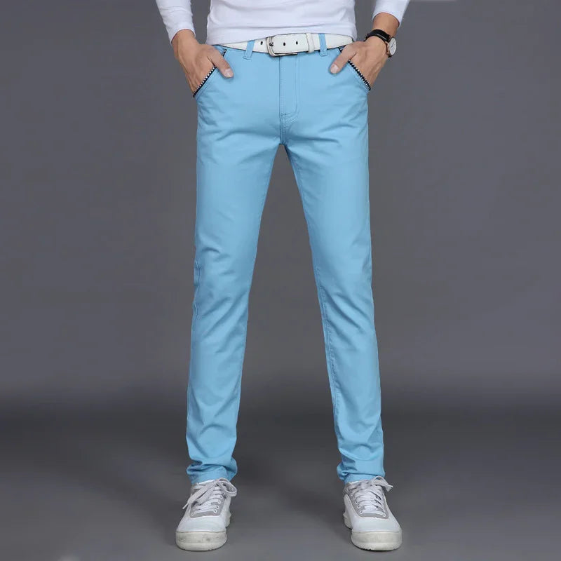 Man wearing light blue slim fit casual pants with white belt and white sneakers on gray background