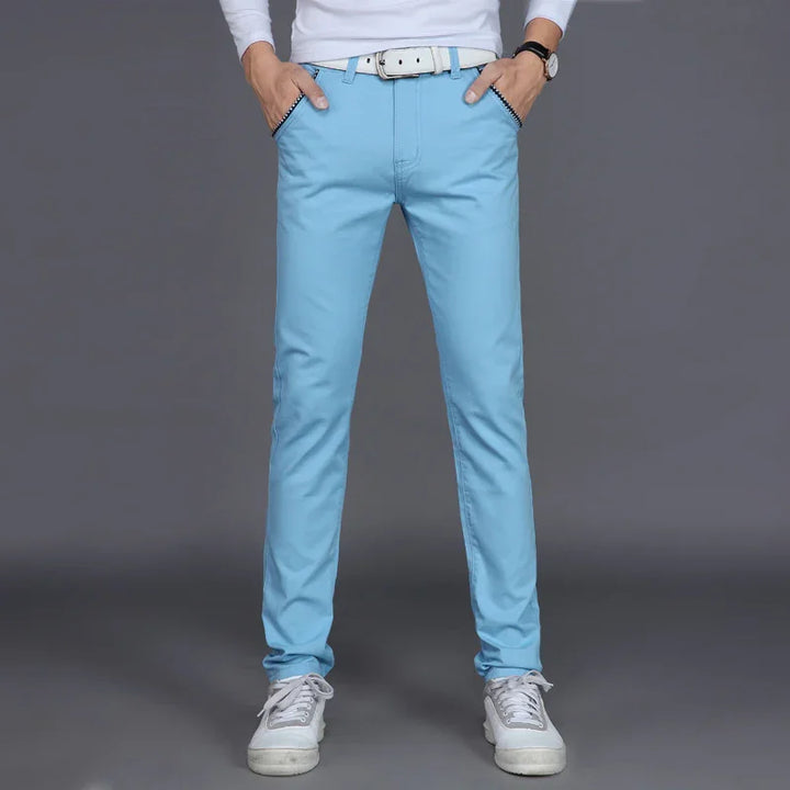 Man wearing light blue slim fit casual pants with white belt and white sneakers on gray background