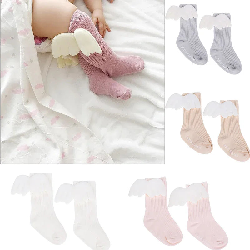 Baby wearing pink angel wing socks lying on white blanket with matching socks in gray, beige, white, and pink