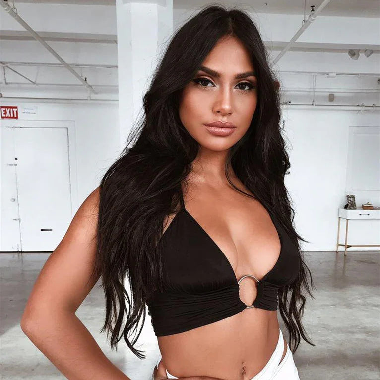 Confident woman with long black hair wearing a black crop top and white pants in a minimalist indoor space